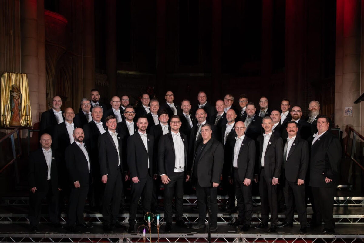 Actually Gay Men's Chorus stood on stage in black suits with white shirts and bow ties.